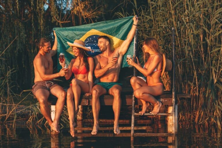 Happy group of young people drinking beer with a Brazilian flag on a dock by the river during the summer sunny day